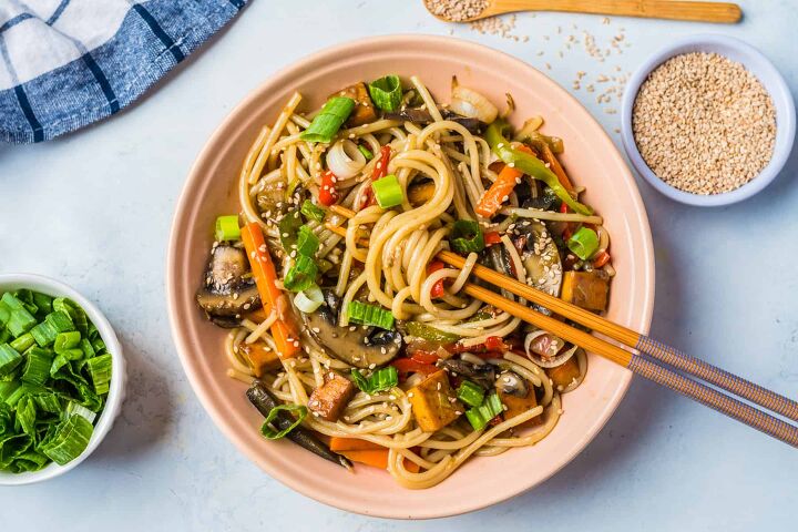 vegan stir fry noodles ready in under 30 minutes, A pink bowl with vegan stir fry noodles with chopsticks and chopped green onion on a side