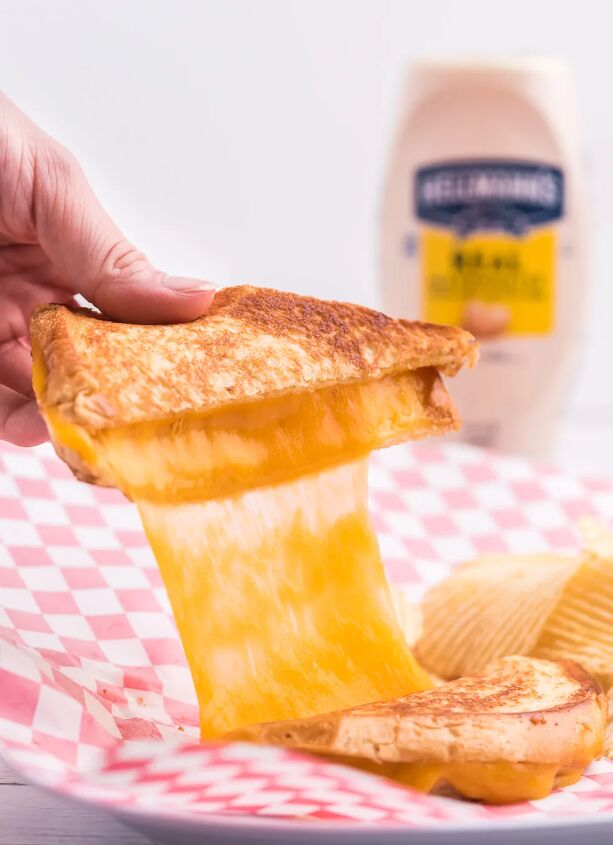 the secret to the perfect grilled cheese sandwich, amazing cheese pull from a simple grilled cheese sandwich being held by a woman s hand Bottle of hellmann s in the background