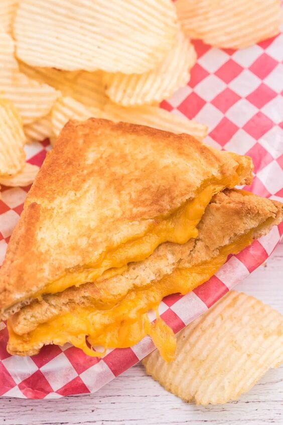 the secret to the perfect grilled cheese sandwich, grilled cheese with extra cheese oozing out of it Served on restaurant style checkered wax paper and ruffled chips