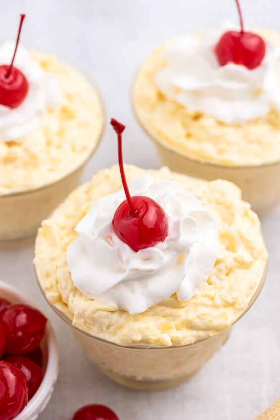 easy pineapple dessert comes together with 3 ingredients, angled down view of pineapple pudding served in individual dishes with whipped cream and a cherry on top