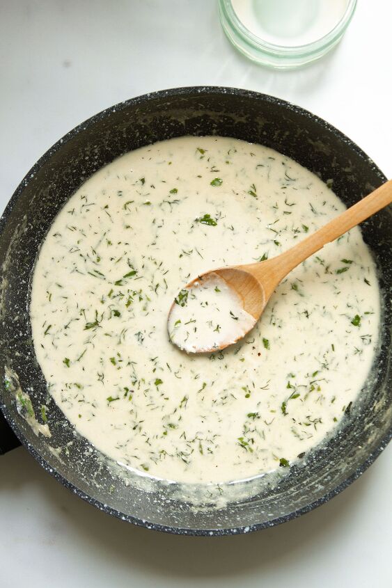 creamy white wine pasta sauce, Adding the Parmesan cheese dill and parsley to the sauce in a pan on a white background