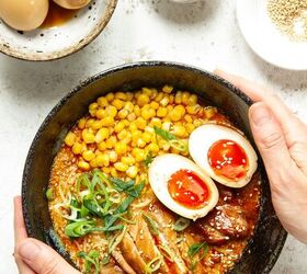 easy spicy chicken miso ramen, Hands holding a bowl of miso ramen on a white background with three additional bowls containing ramen eggs sesame seeds and sliced scallions