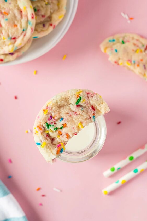 soft and chewy funfetti cookies recipe, Half of a confetti cookie on top of a glass of milk next to straws and more cookies