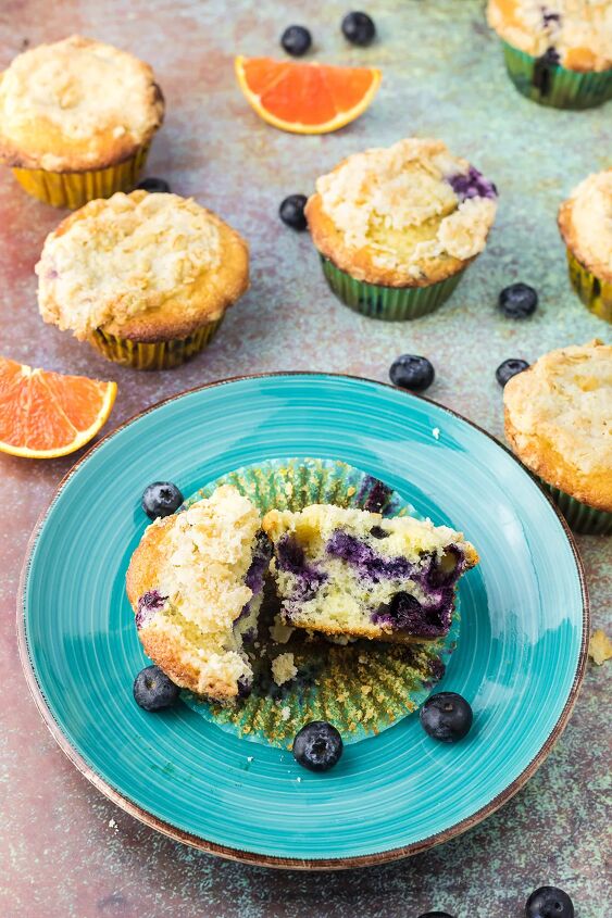 blueberry orange muffins with crunchy oat topping, Orange blueberry muffin broken open on blue plate More muffins around it on a table