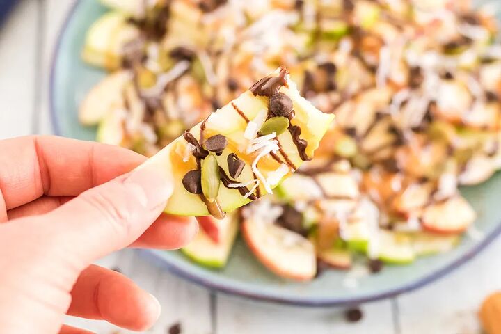 crunchy apple nachos with sweet and salty toppings, Holding an apple nacho above a plate of apple slices with toppings