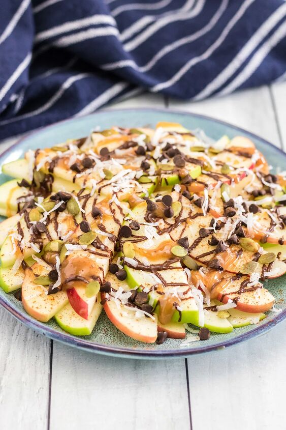 crunchy apple nachos with sweet and salty toppings, Plate full of apple nachos topped with chocolate caramel and nuts with a blue napkin on the table