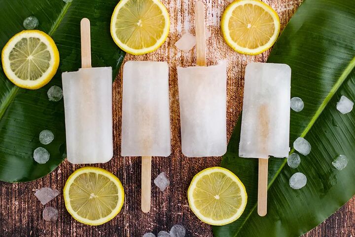 easy and refreshing lemon popsicles, Four lemon popsicles in a row on a table with greens and lemon slices