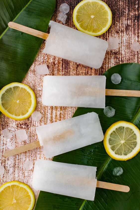 easy and refreshing lemon popsicles, Four ice pops on a table with ice cubes leaves and lemon slices