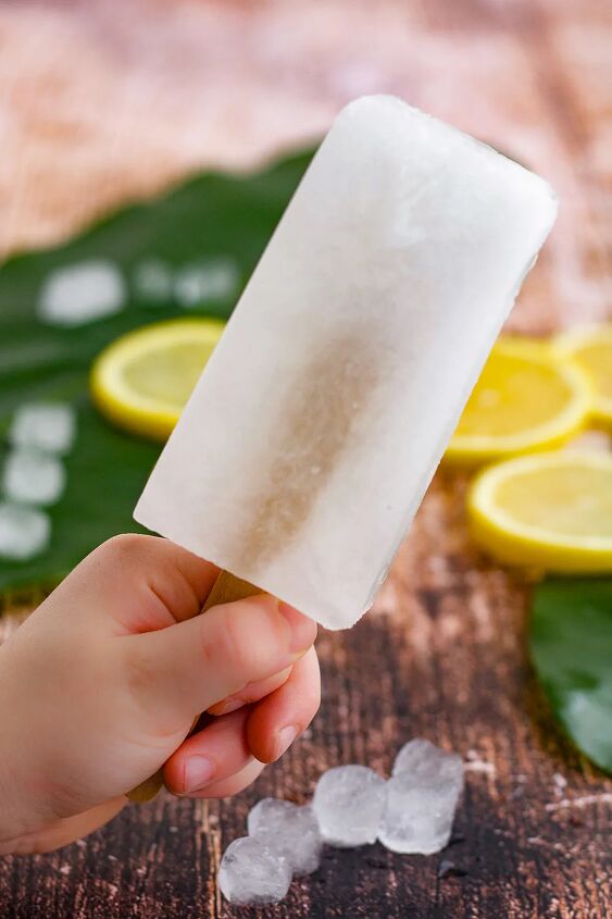 easy and refreshing lemon popsicles, Holding a lemon ice pop with slices in the background
