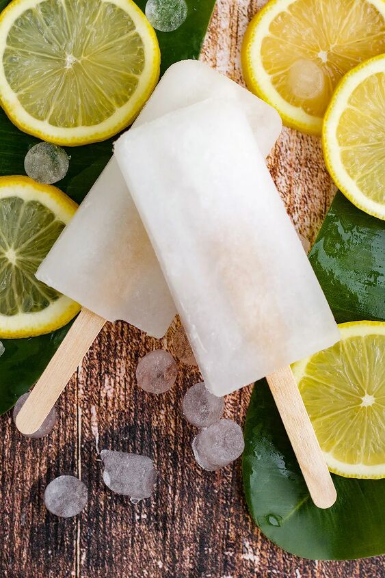 easy and refreshing lemon popsicles, Two lemon pops on top of each other with lemon slices and nugget ice on the table