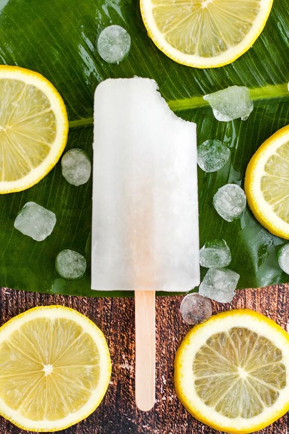 easy and refreshing lemon popsicles, One frozen lemon pop with a bite missing with lemon slices on the table