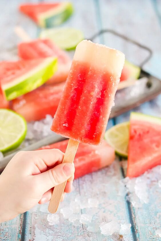 fresh watermelon popsicles recipe, Holding a red popsicle with more pops in the back on a tray