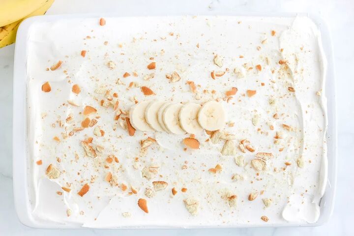 light and creamy banana poke cake recipe, Top of cake topped with white frosting and cookie crumbles