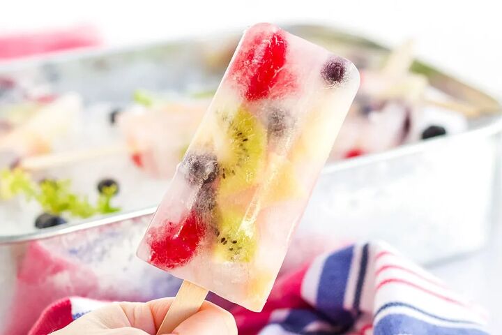 rainbow fruit popsicles, Holding a fruit popsicle with more fresh fruit pops in the background