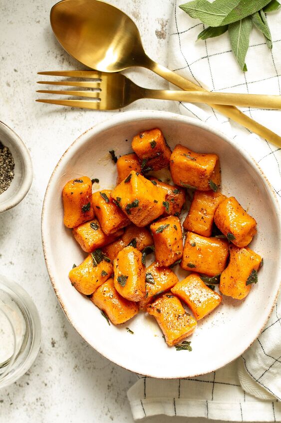 sweet potato gnocchi with brown butter and sage, A bowl of sweet potato gnocchi and sage leaves with a fork and spoon on a white table and white check cloth background
