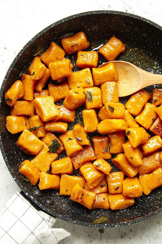 sweet potato gnocchi with brown butter and sage, Tossing the cooked gnocchi in the sage butter sauce in a frying pan on a white background