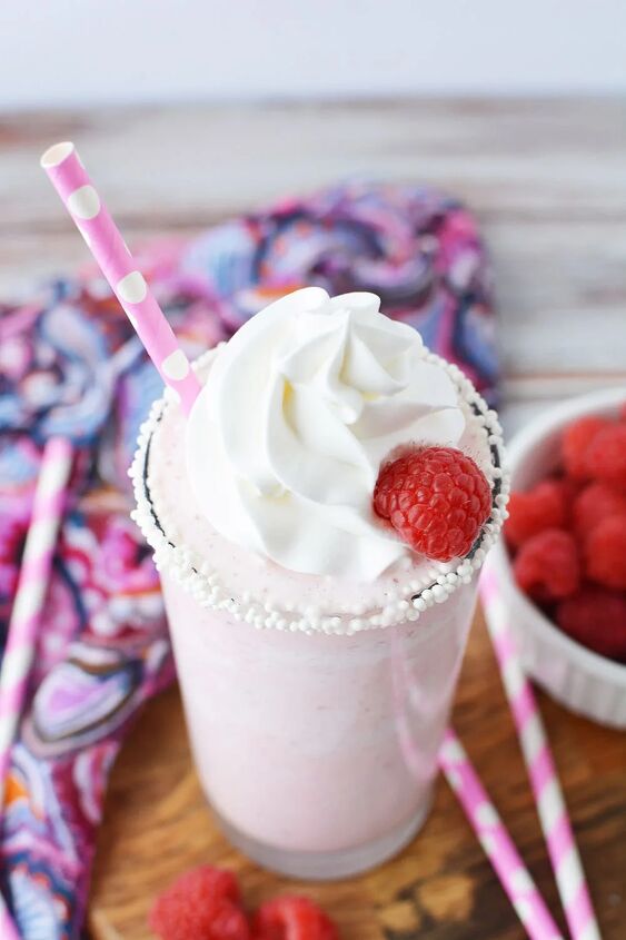 copycat raspberry cotton candy frappuccino recipe, Tilted glass of raspberry frappe next to pink straws and fresh raspberries