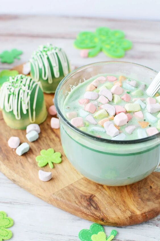 glittery green hot chocolate bombs recipe, Glass mug of green hot cocoa on a board with cocoa bombs sitting next to it
