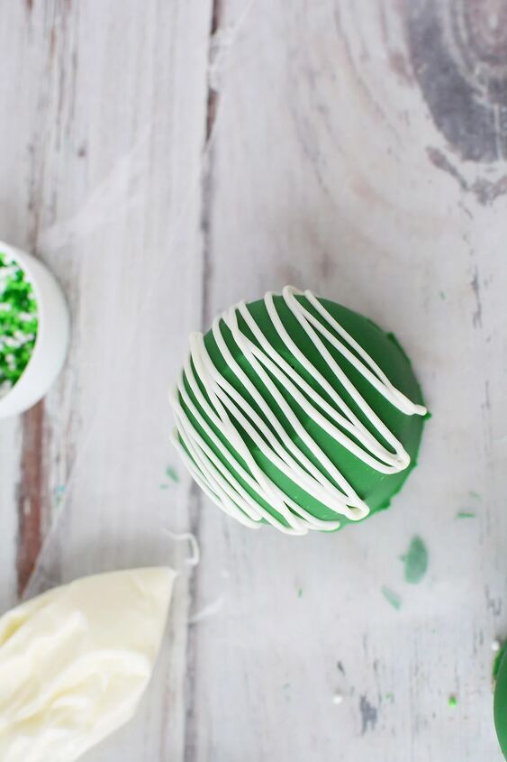 glittery green hot chocolate bombs recipe, Green cocoa bomb on waxed paper to drizzle white candy topping