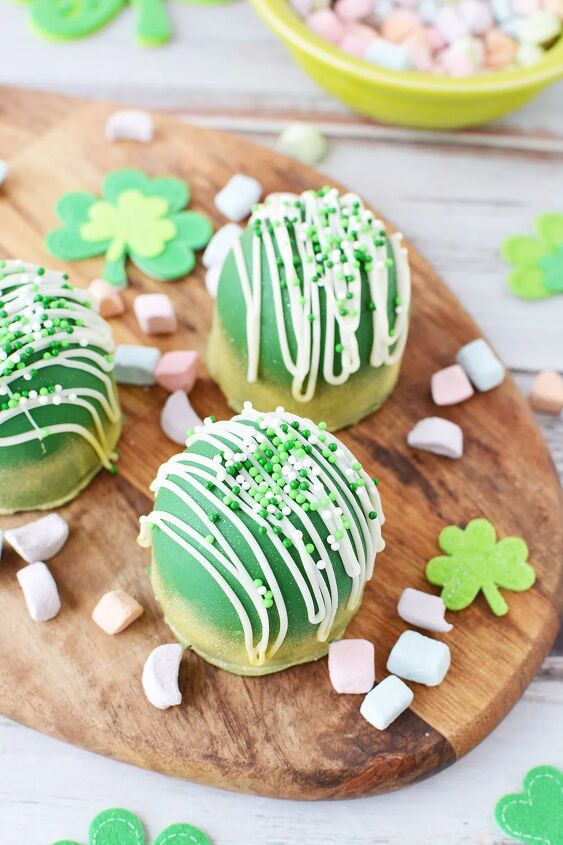 glittery green hot chocolate bombs recipe, Green chocolate bombs sitting on a board with rainbow marshmallows and St Patrick s Day decorations