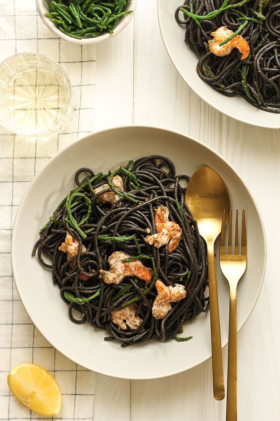 black squid ink pasta, Two white plates of black squid ink pasta topped with samphire and cooked prawns with a small dish of samphire and a slice of lemon