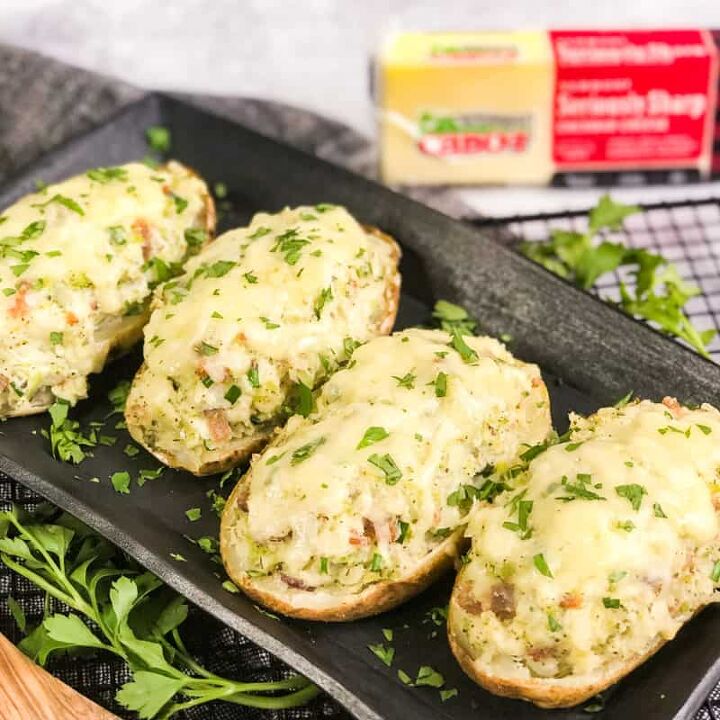 air fryer twice baked loaded potatoes, Overhead shot of Air Fryer Twice Baked Loaded Potatoes garnished with parsley on a black serving platter with a block of Cabot Seriously Sharp Cheddar Cheese in forground