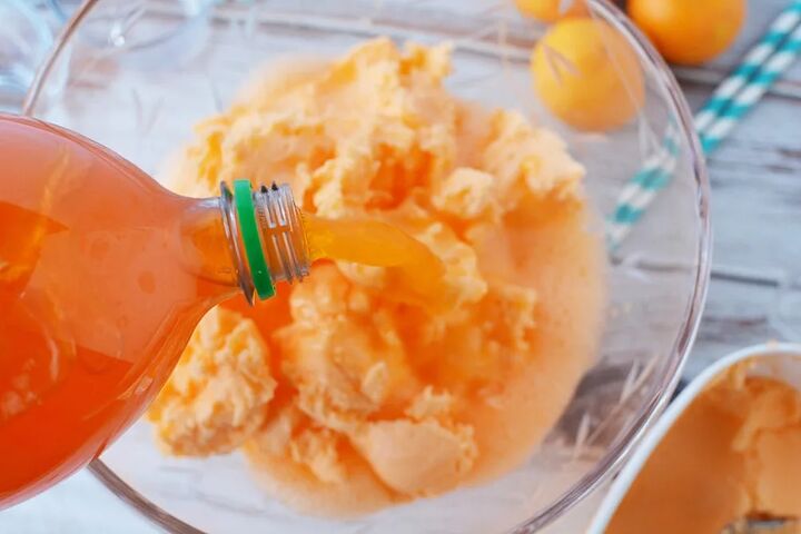 easy orange sherbet punch recipe, Pouring orange soda into punch bowl with sherbet