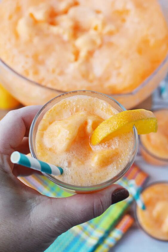 easy orange sherbet punch recipe, Holding up a glass of orange punch with an orange slice above bowl