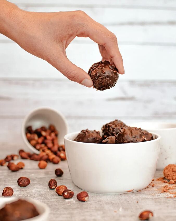 homemade chocolate coconut date balls, Holding a date ball above other coconut balls and hazelnuts in the background