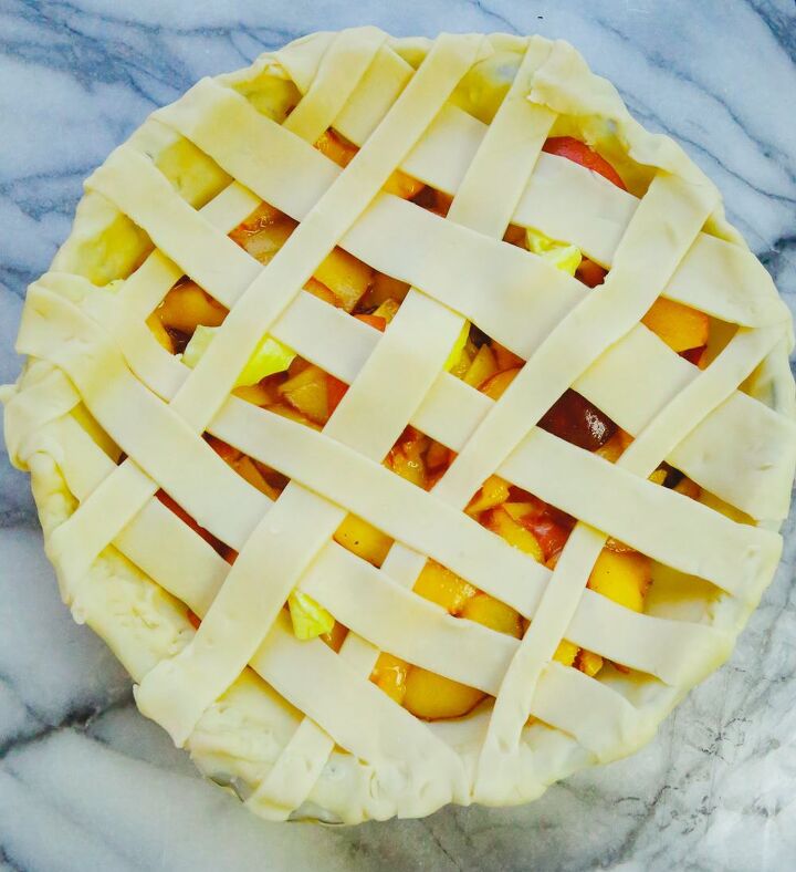 honey peach pie homemade, lattice pie crust topping with fresh peaches in a glass pie dish on a marble slab