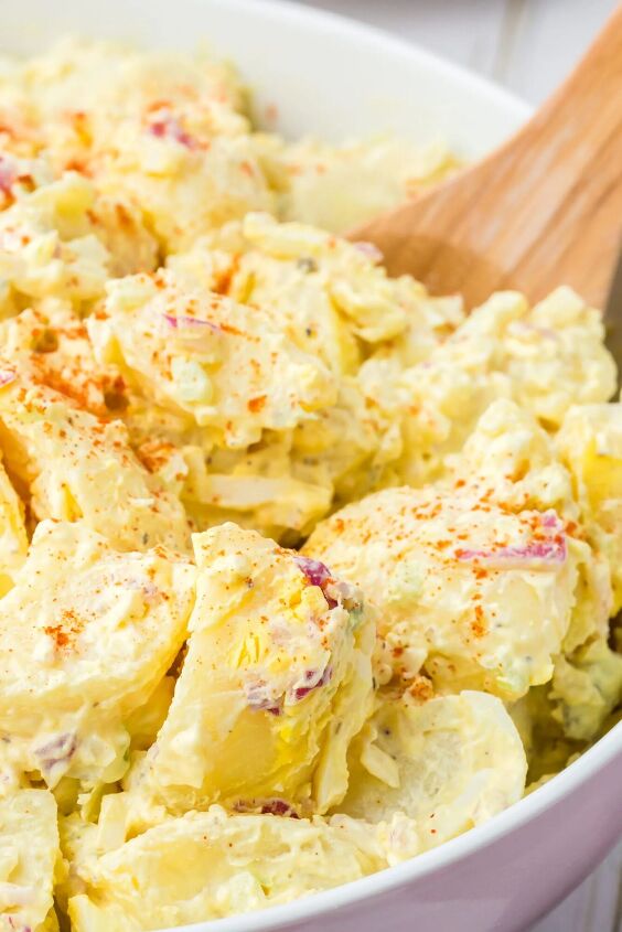 how to make traditional potato salad recipe this weekend, up close angled down view of a bowl of potato salad with a spoon topped with paprika garnish