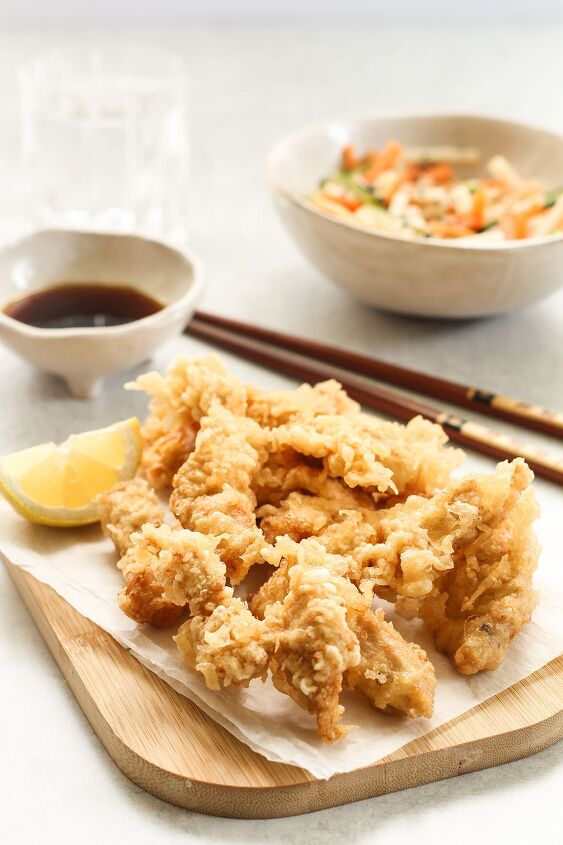 japanese chicken tempura with light and crispy batter, Chicken Tempura with a slice of lemon on a wooden board and a bowl of ponzu dipping sauce a salad bowl and chopsticks in the background