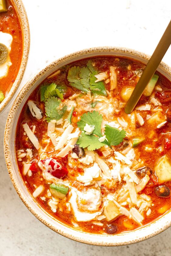easy spicy mexican chilli bean soup with corn, Close up of a bowl of Mexican Bean Soup on a white table background with cheese cilantro and avocado toppings