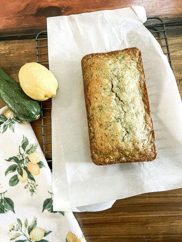 the best lemon zucchini bread, bread on a cooling rack on table with lemon and zucchini