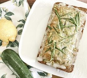 the best lemon zucchini bread, loaf of zucchini bread with glaze on a white plate with fresh zucchini and lemon