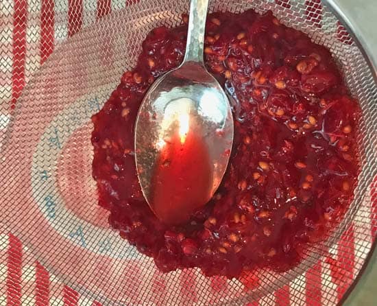 pressing red currants through a metal strainer with a spoon to extract the juice