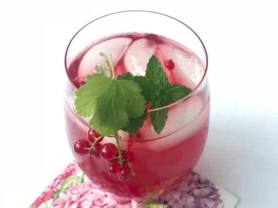 Finished glass of red currant honey iced tea garnished with fresh currants and currant leaves