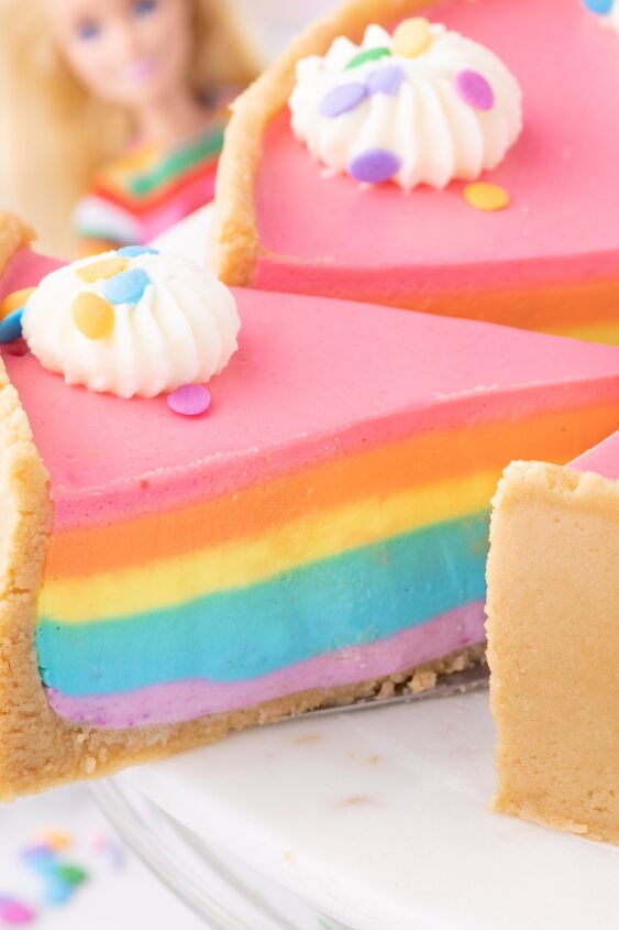 how to make a show stopping barbie no bake rainbow cheesecake, slice being removed from barbie rainbow cake