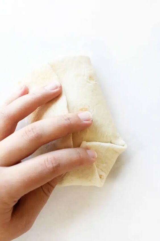 how to make beef chimichanga quick and easy, A hand holding a folded chimichanga before baking