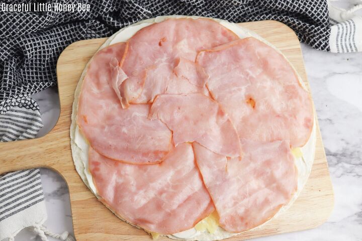Tortilla cream cheese and pineapple being layered with sliced deli ham