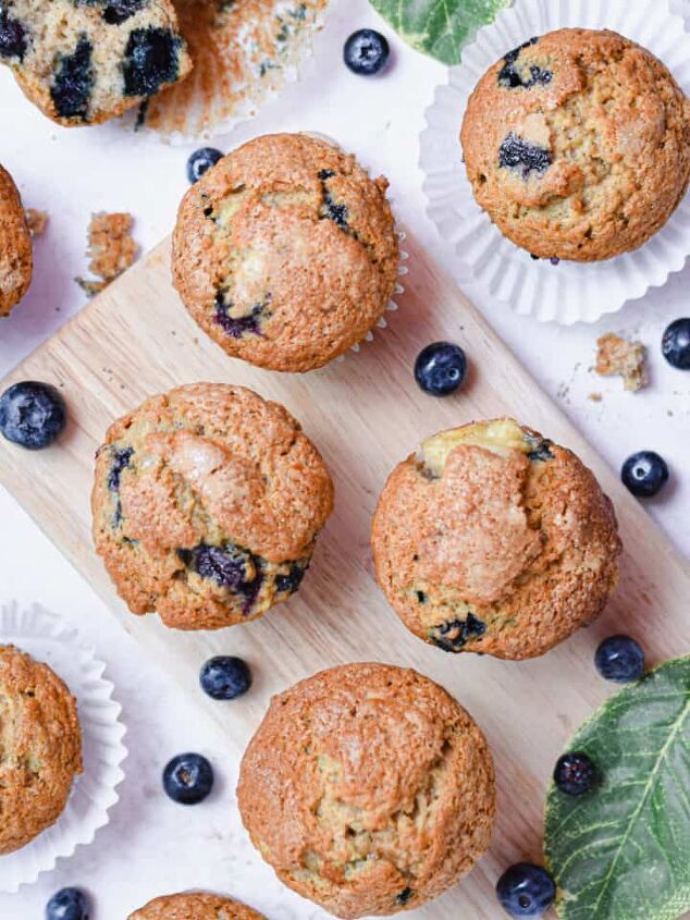simple 3 ingredient banana oatmeal bars, A group of banana blueberry muffins are on a cutting board with leaves and blueberries around them
