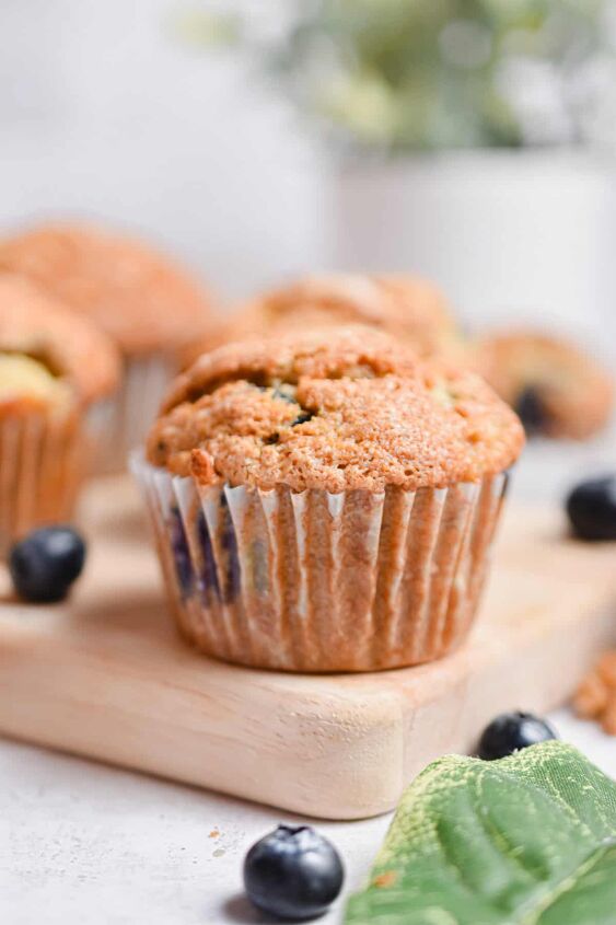 the best banana blueberry muffins so moist, One banana blueberry muffin is on a cutting board with a plant in the background