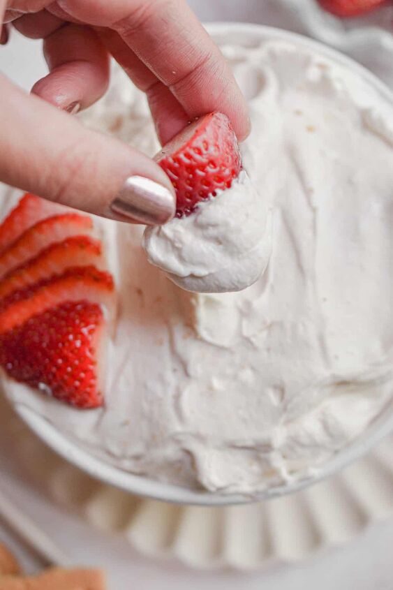3 ingredient strawberry fluff fruit dip so easy, A hand is holding a strawberry that was just dipped in the 3 ingredient strawberry fluff dip