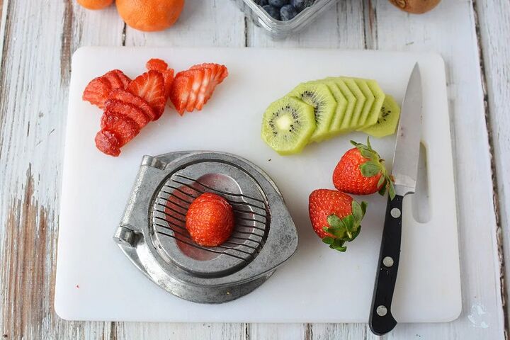fresh fruit pizza dessert with ice cream cone crust, Sliced strawberries and kiwis on a cutting board with a knife and a fruit slicer