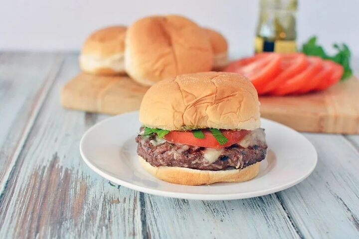 juicy grilled italian burger recipe, Grilled Italian burger on a plate with tomatoes and buns in the background