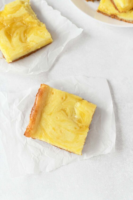 lemon curd cheesecake bars, Lemon Swirled Cheesecake cut and on pieces of white parchment paper