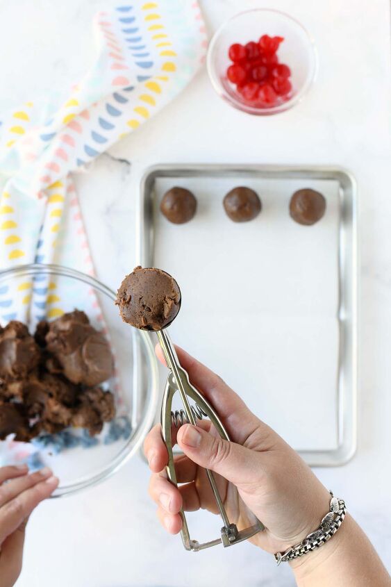 chocolate covered cherry brownie truffles, A white hand holding a cookie scoop with brownie dough in it