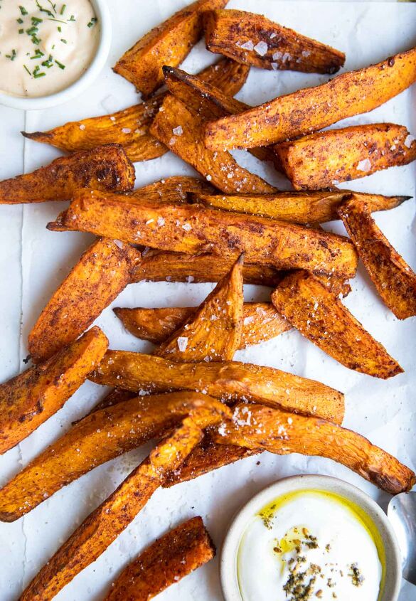 air fryer sweet potato wedges, crispy air fryer sweet potato wedges sprinkled with sea salt and sitting on a piece of parchment paper next to dipping sauces