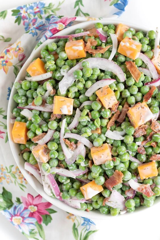how to make classic pea salad, up close view of pea salad with creamy dressing cheddar cheese chunks onion slivers and chopped bacon