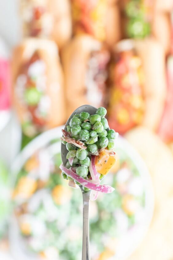 how to make classic pea salad, up close view of spoonful of classic summer pea salad with cheese chunk slivered onions and bacon bits